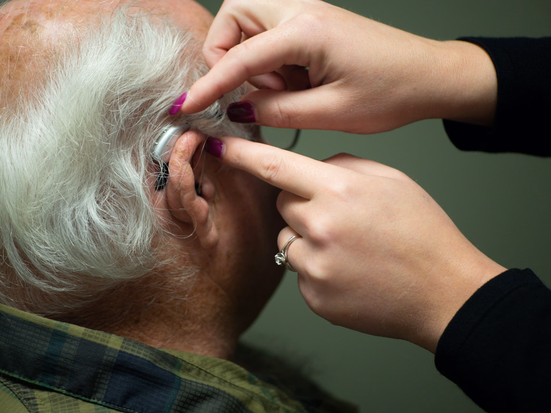Close-up of a hearing aid being fitted to an older adult's ear
