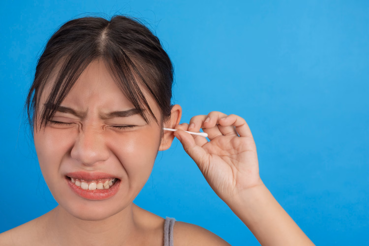 A person wincing while pushing a cotton swab into their ear